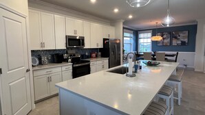 Una cocina moderna con armarios blancos, electrodomésticos de acero inoxidable y una isla central con taburetes de bar.