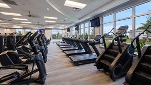 Un gimnasio con numerosas cintas de correr y equipo de ejercicio, amplias ventanas y un ventilador de techo.