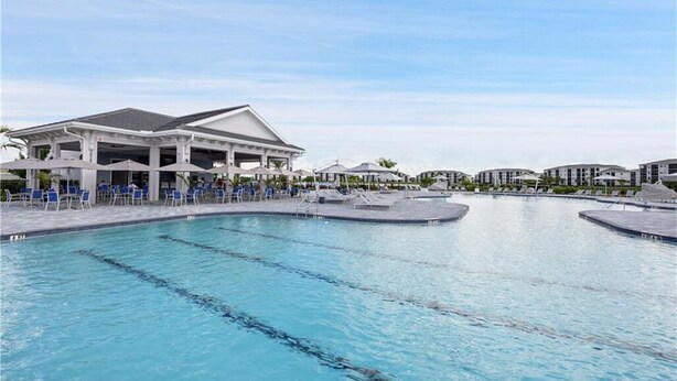 Una piscina con sillones de playa y sombrillas, un pabellón cubierto y edificios modernos al fondo.