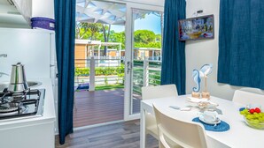 A compact kitchen with a gas stove, a sink, and a window with blue curtains. - Cosy apartment in villa for 3 guests with WIFI, pool, A/C, TV and patio (Castiglione Della Pescaia)