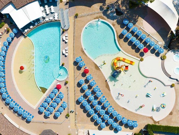 Luchtbeeld van een resort met twee grote zwembaden, ligbedden en een waterglijbaan.