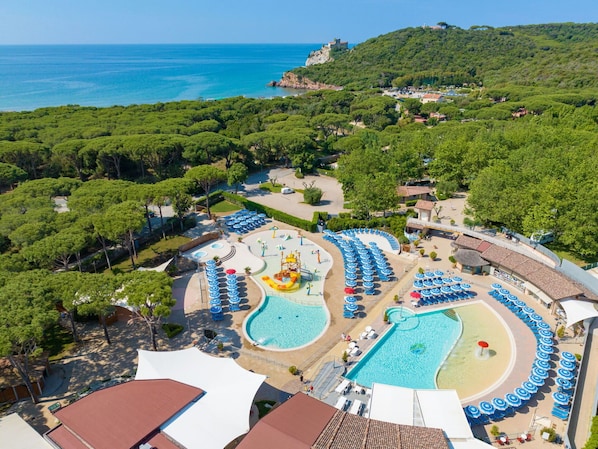 An aerial view of a resort with multiple swimming pools, sun loungers, and a view of the sea.