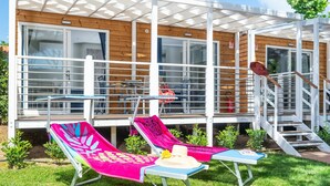 A modern outdoor lounge area with two sun loungers, a small table, and a staircase leading to a wooden deck. - Cosy apartment in villa for 4 guests with WIFI, A/C, pool, TV and terrace (Castiglione Della Pescaia)