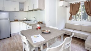A modern kitchen with white cabinets, a built-in stove, and a dining area with a wooden table and white chairs. - Cosy apartment in villa for 4 guests with WIFI, A/C, pool, TV and terrace (Castiglione Della Pescaia)