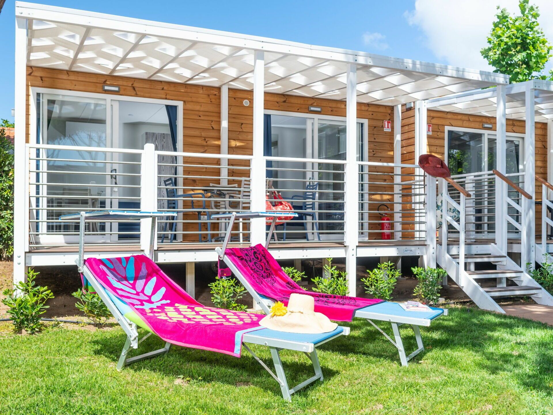 Un espace de détente extérieur moderne, comprenant deux chaises longues, une petite table et un escalier menant à une terrasse en bois.