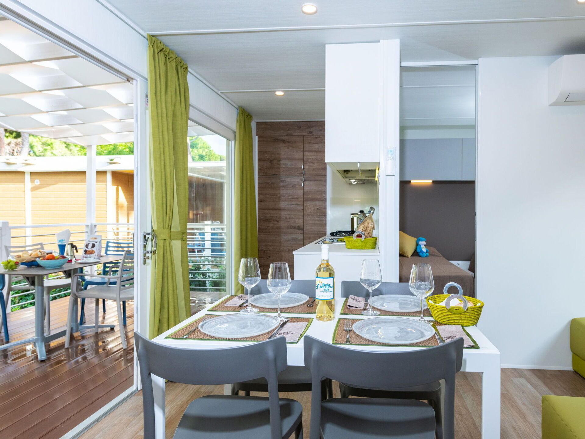 Un comedor moderno con una mesa dispuesta para cuatro personas, una zona de cocina con estufa y vistas a una terraza de madera.