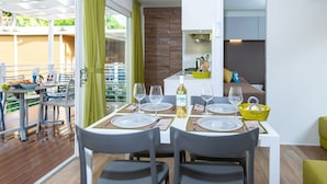 A modern dining area with a table set for four, a kitchen area with a stove, and a view of a wooden deck. - Cosy apartment in villa for 4 guests with WIFI, A/C, pool and terrace (Castiglione Della Pescaia)