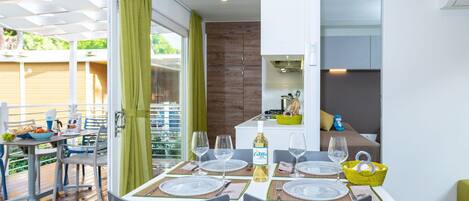 Un comedor moderno con una mesa dispuesta para cuatro personas, una zona de cocina con estufa y vistas a una terraza de madera.