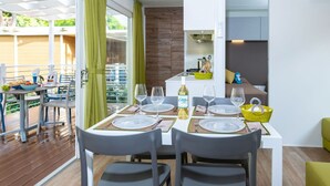 Een moderne eetruimte met een tafel voor vier personen, een keuken met fornuis, en uitzicht op een houten terras.