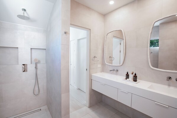 A modern bathroom with a shower, a sink with a mirror, and a door leading to another room. - Palm Grove (Holetown)