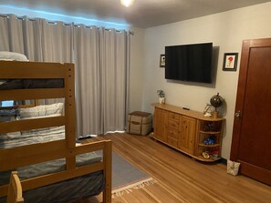 A room with a bunk bed, a TV mounted on the wall, a wooden cabinet with various items, and a door.