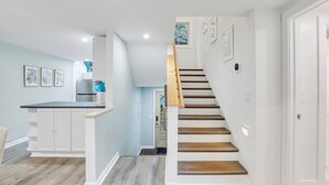 Une cuisine moderne avec des meubles blancs, un plan de travail noir et un escalier en bois menant à un deuxième étage.
