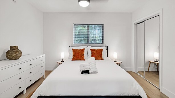 Een moderne slaapkamer met een bed, nachtkastjes, een spiegel en een raam met zonwering.
