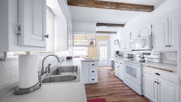 A modern kitchen with white cabinets, stainless steel appliances, and a wooden ceiling beam.