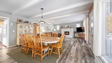A spacious dining area with a round wooden table and chairs, a chandelier, and a fireplace.