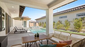 A covered outdoor area with a pool, lounge chairs, a table, and a sofa. - Play Paradise: Pool+Spa, BBQ, GameRoom, PGA West! (La Quinta)