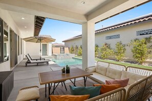 A covered outdoor area with a pool, lounge chairs, a table, and a sofa. - Play Paradise: Pool+Spa, BBQ, GameRoom, PGA West! (La Quinta)