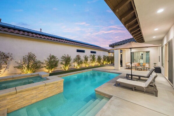 A modern outdoor pool area with a hot tub, lounge chairs, and a covered seating area.