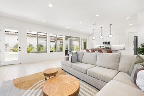 A modern living room with a sofa, a coffee table, and a kitchen area in the background. - Play Paradise: Pool+Spa, BBQ, GameRoom, PGA West! (La Quinta)