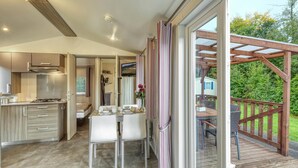 A modern kitchen with a dining area, a small bedroom, and a wooden deck with outdoor seating. - Pet friendly (sta)caravan in Irrhausen (Irrhausen)