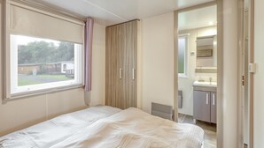 A bedroom with a bed, a window, a wardrobe, and a bathroom visible through an open door. - Pet friendly (sta)caravan in Irrhausen (Irrhausen)