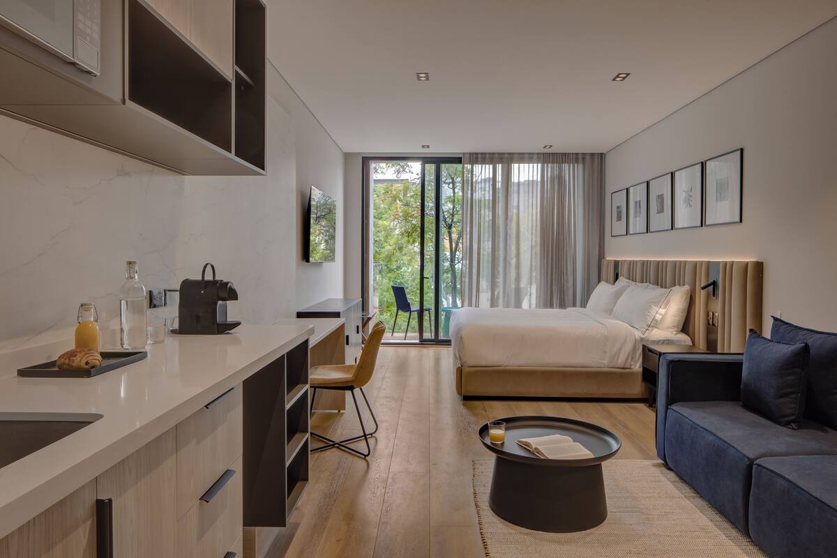 Una habitación de hotel moderna con kitchenette, una cama, un sofá y un ventanal grande.