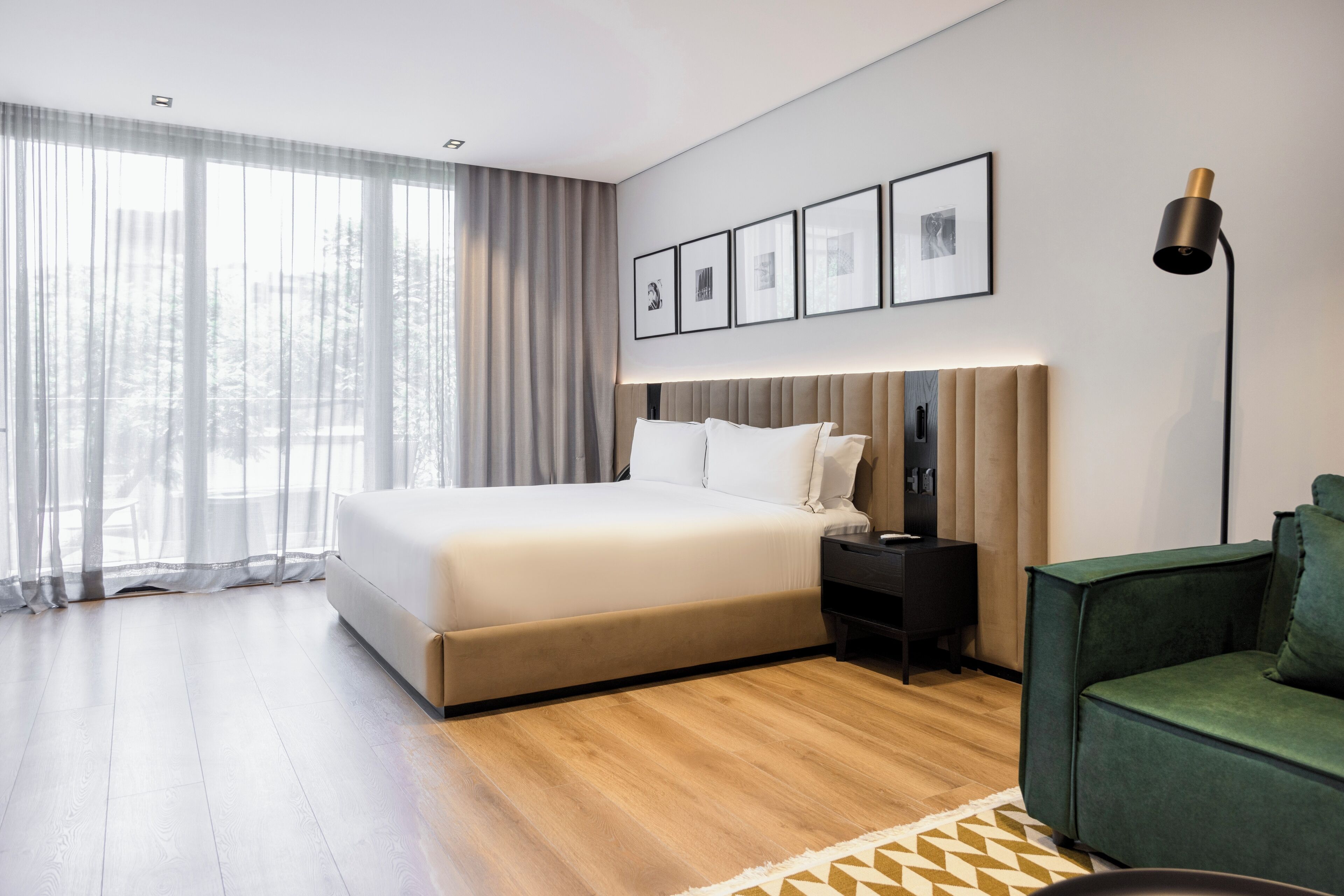 A modern bedroom with a large bed, a nightstand, a green sofa, and a large window with sheer curtains.