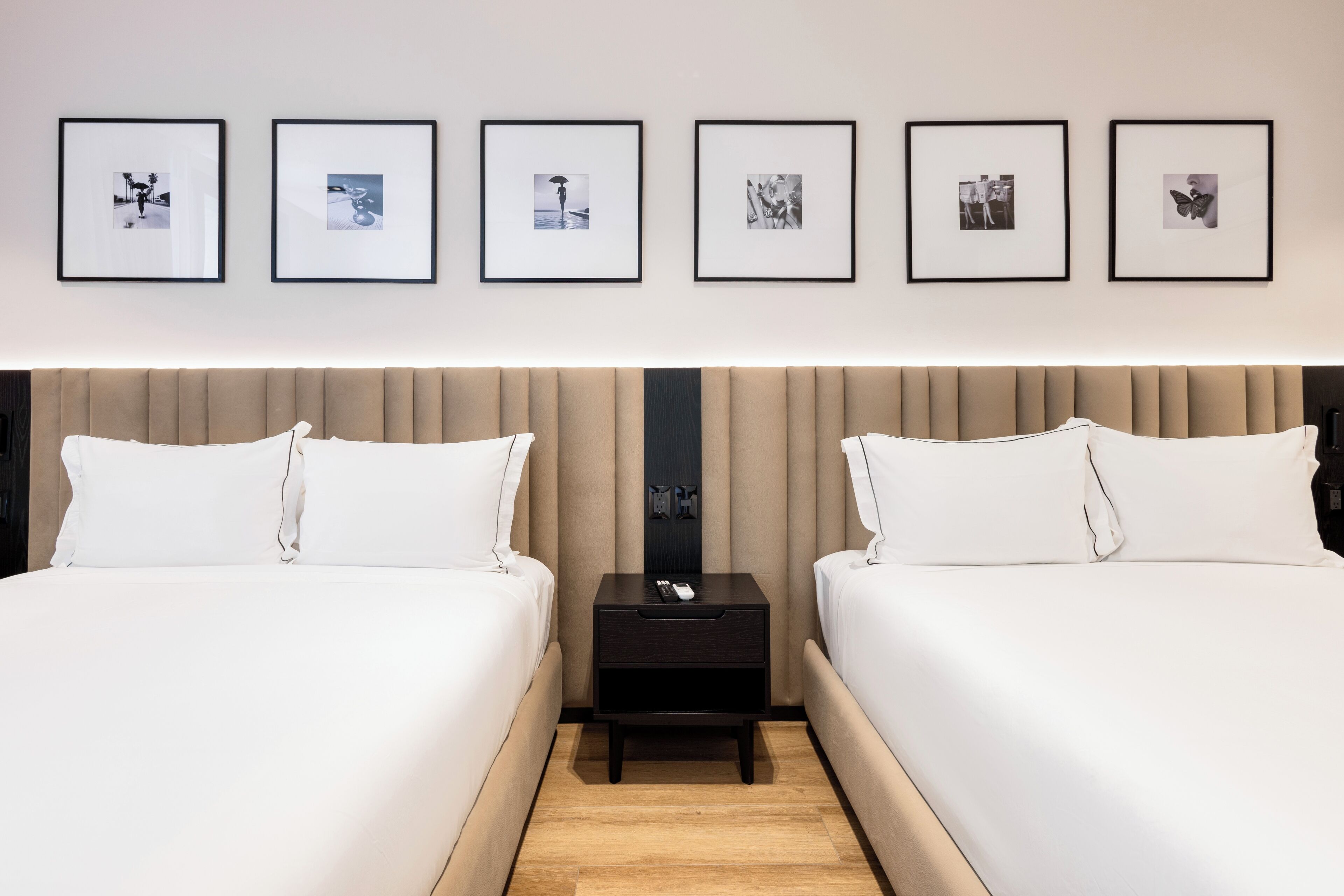 A hotel room with two beds, a nightstand, and a wall with six framed pictures.