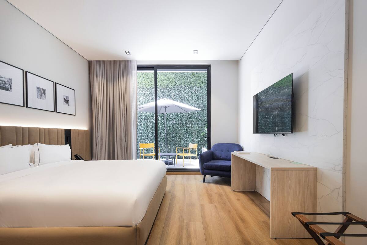 Una habitación de hotel moderna con una cama grande, un escritorio, una silla, un televisor y un balcón con sombrilla.