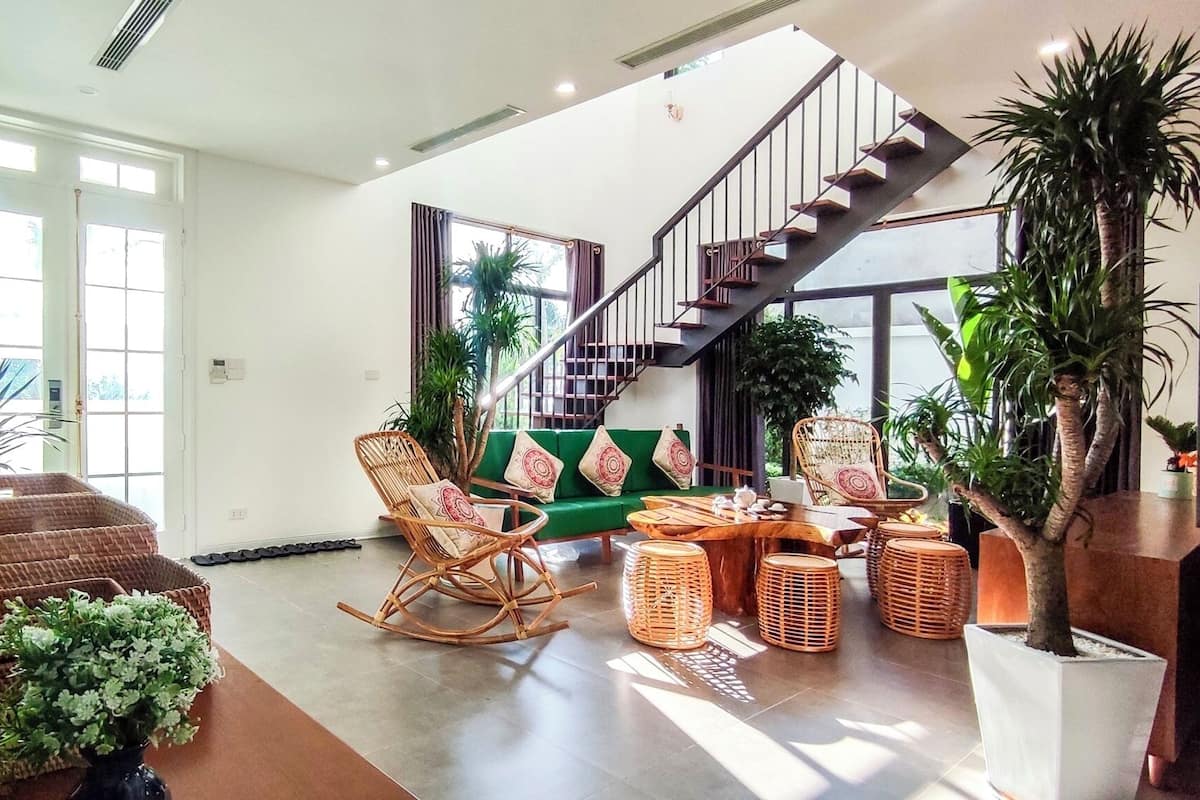 A spacious living area with a green sofa, wicker chairs, a wooden coffee table, and a staircase leading to an upper floor.