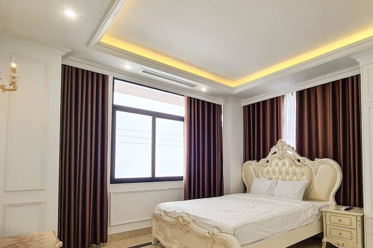 A bedroom with a large bed, white wardrobe, and a window with curtains.