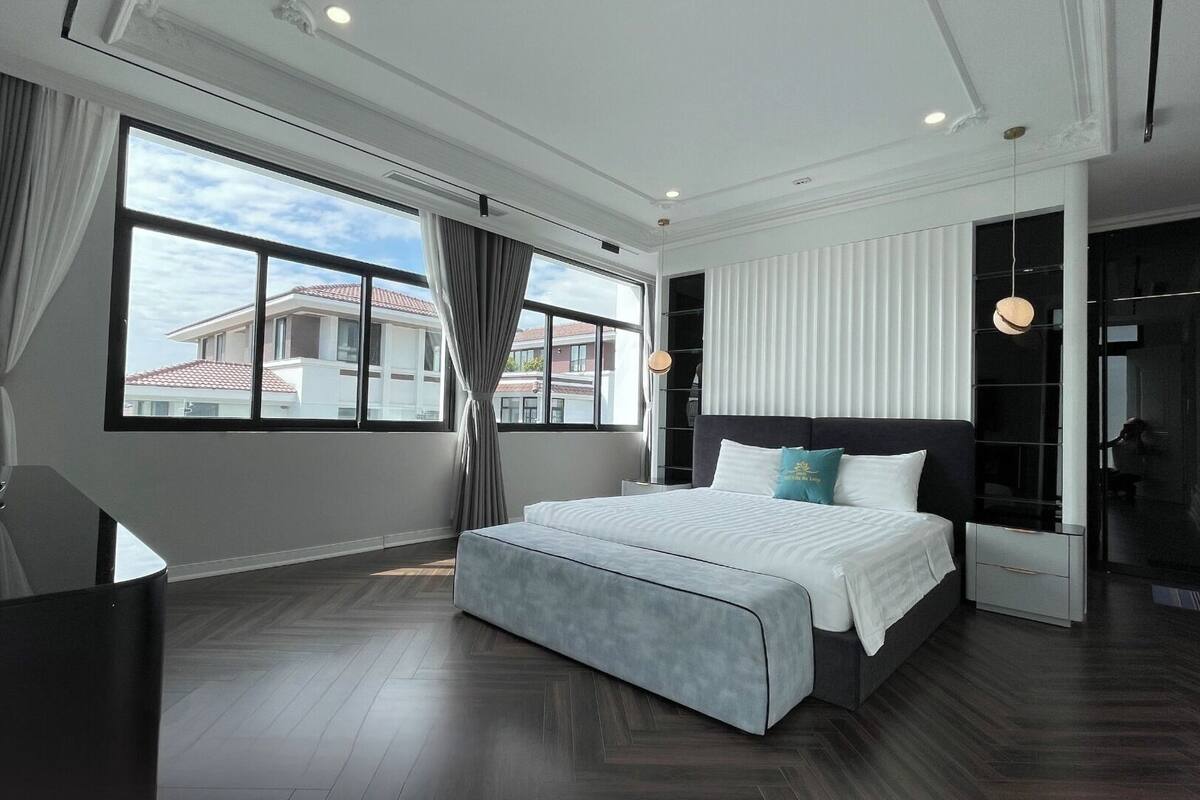 A modern hotel room with a large bed, a desk, and a view of buildings outside.