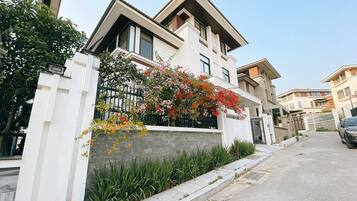 A modern two-story house with a stone facade, a balcony with flowering plants, and a gated entrance.