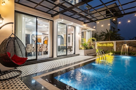 A modern outdoor pool area with a glass-enclosed patio, a hanging chair, and a sign reading 'Cafe on the Villa.'