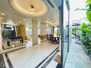 A modern hotel lobby with a marble floor, a reception desk, and a dining area with wooden chairs and a table.