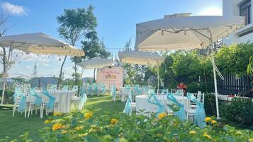 An outdoor event space with tables and chairs, covered by large umbrellas, and a banner in the background.
