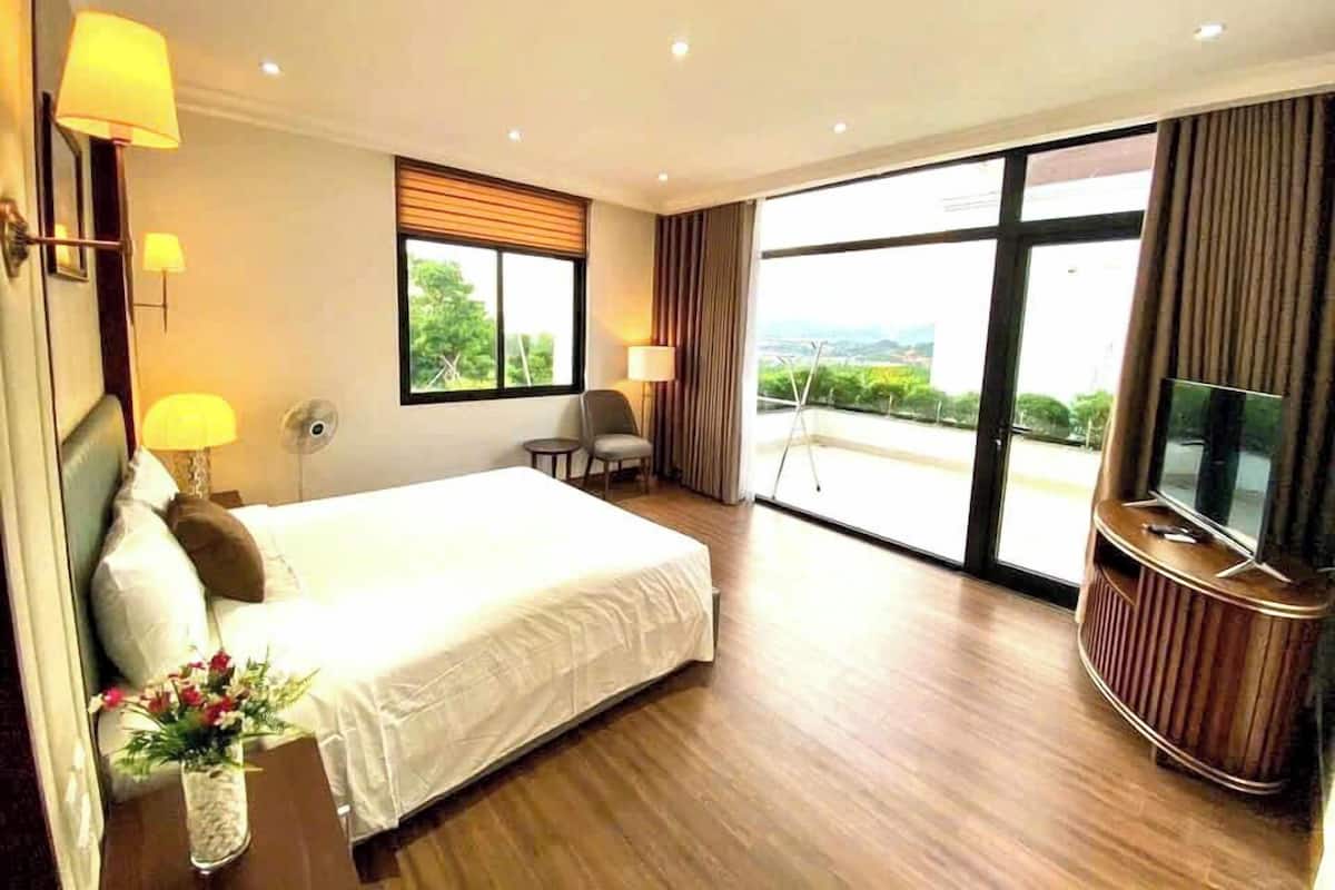 A hotel room with a large bed, a TV, a chair, and a balcony with a view.