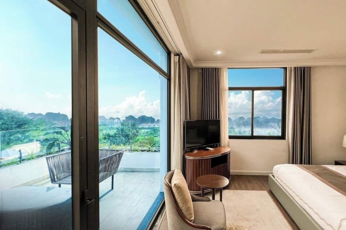 A hotel room with a large window, a bed, a TV, a chair, and a small table.