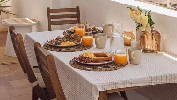 Mesa de desayuno lista, con vista a un paisaje montañoso y una lámpara colgante.