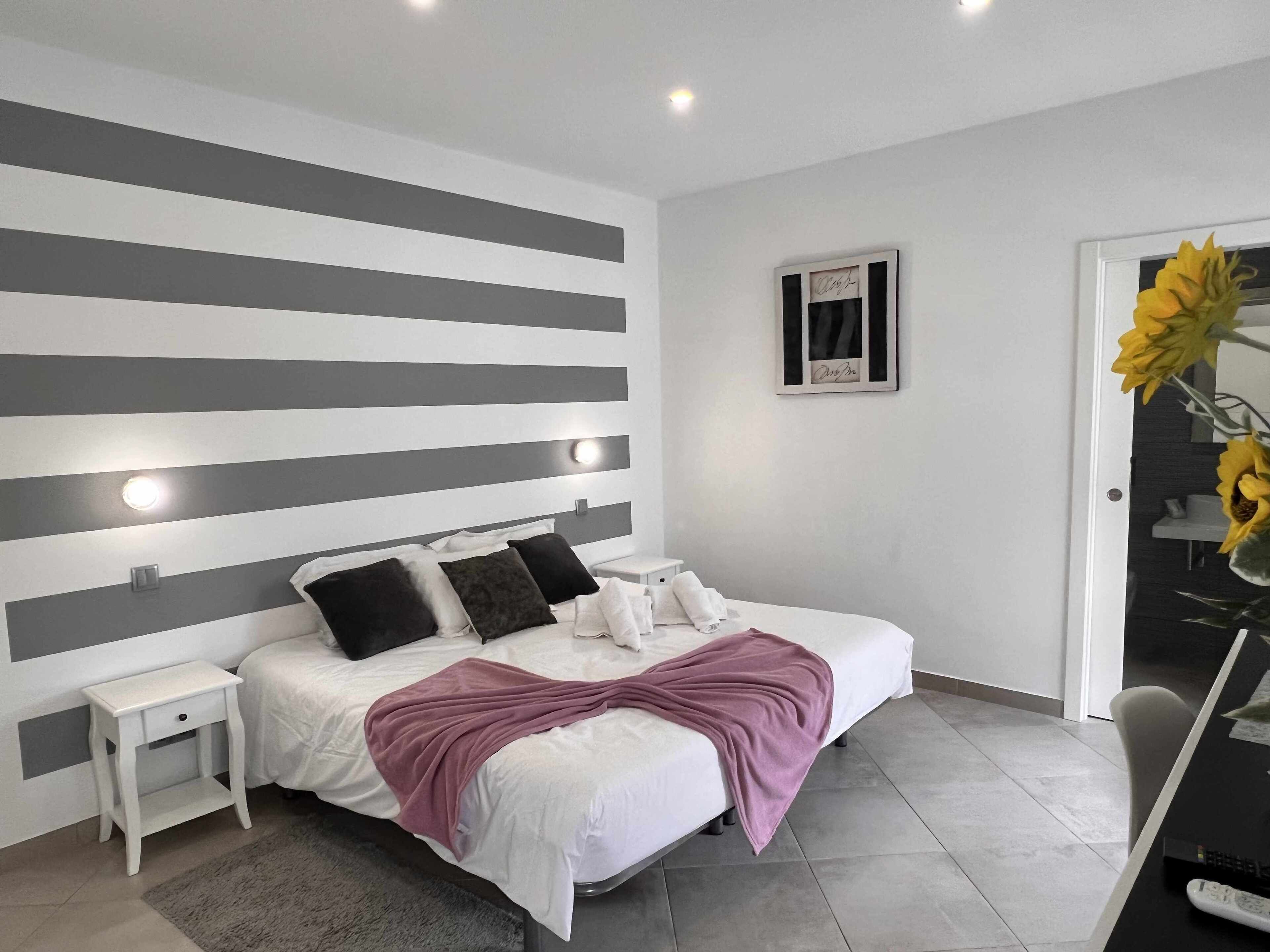 Een moderne slaapkamer met een bed, nachtkastjes, een tafeltje en een vaas met bloemen.