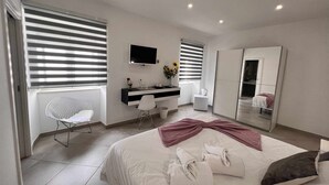 Et moderne hotelværelse med seng, skrivebord, stol, fjernsyn og et stort spejl.
