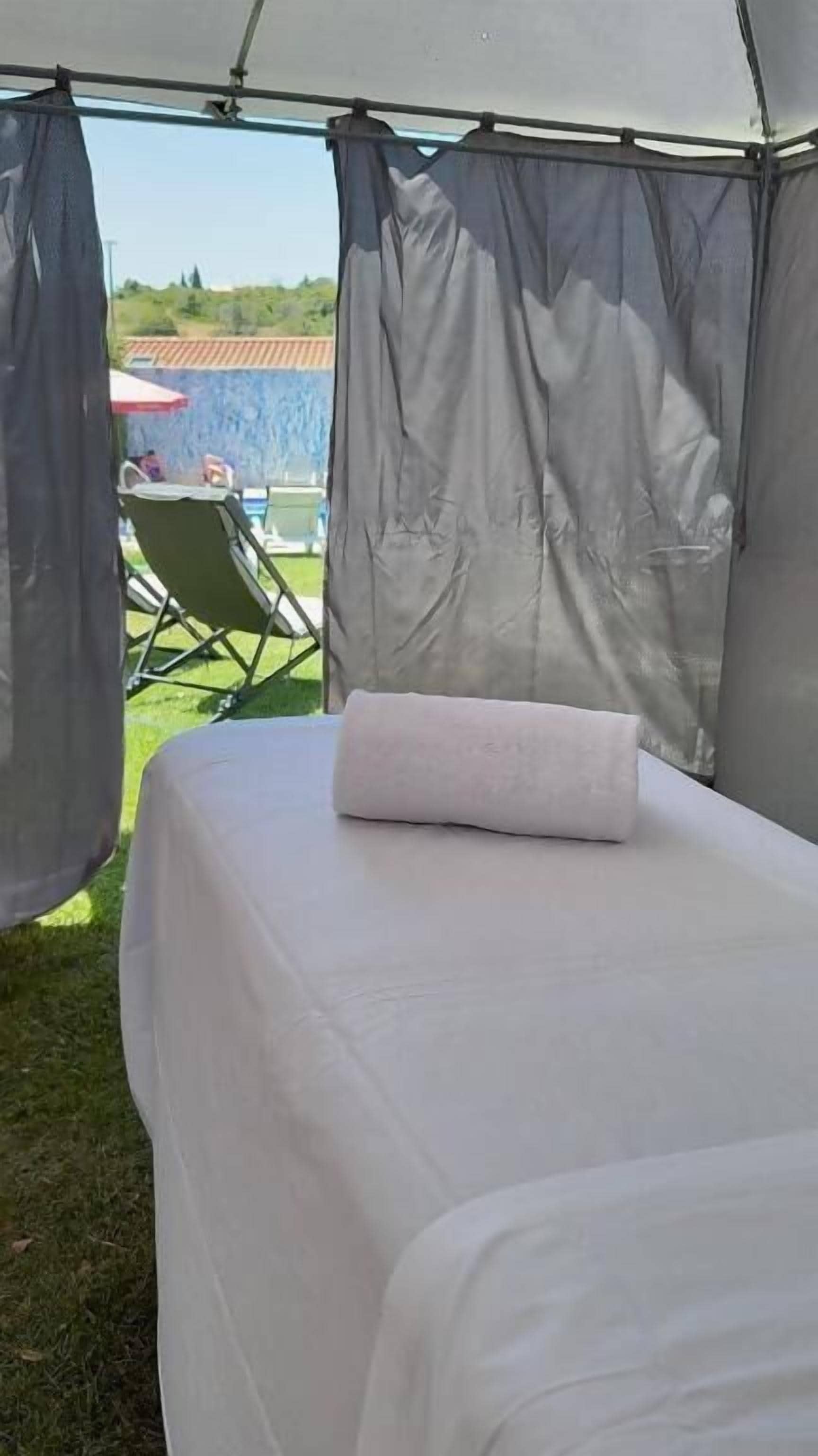 A tented room with a bed, white bedding, and a view of a garden and building outside.