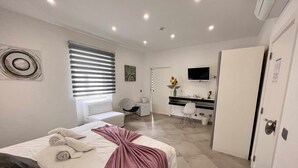 A modern hotel room with a neatly made bed, a small desk with a chair, a TV mounted on the wall, and a bathroom visible through an open door. - Spa Suite 3: Pool, Jacuzzi & Sauna (Poço Partido)