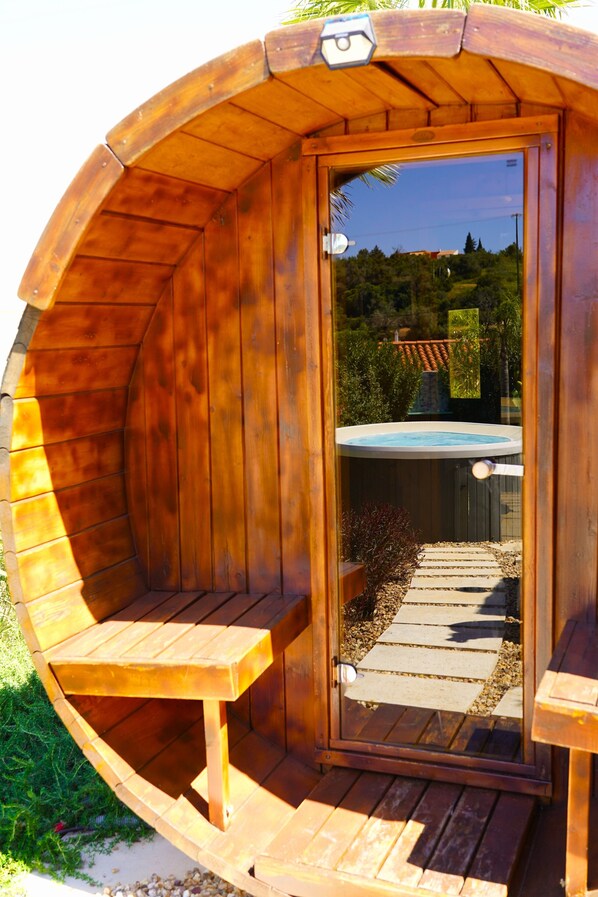 A wooden hot tub with a glass door, a wooden bench, and a stone pathway leading to a backyard.