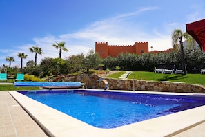A swimming pool with a stone wall, palm trees, and a castle-like building in the background.