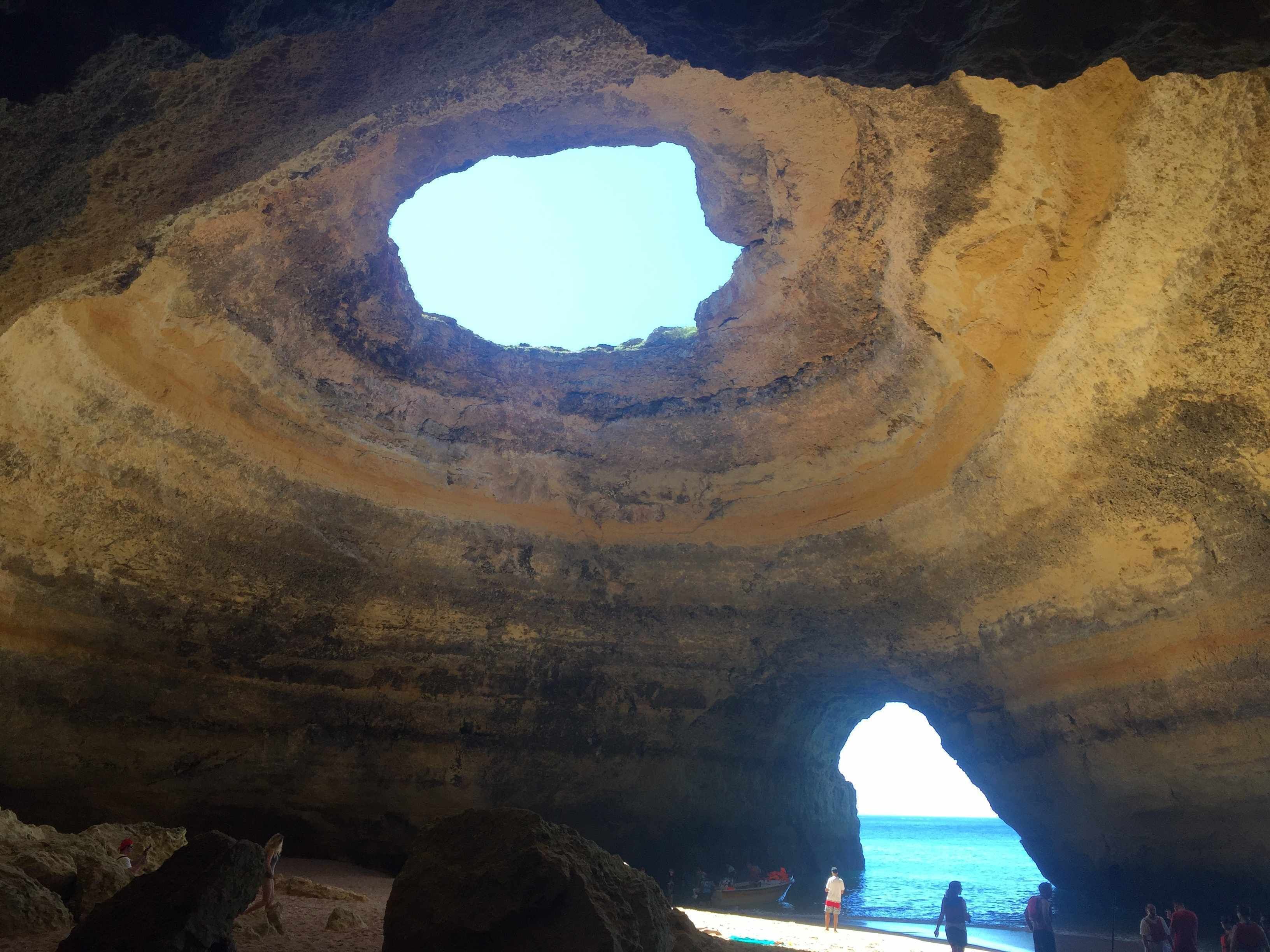 A natural rock formation with a circular opening and a view of the sea through an archway.