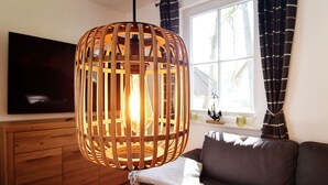 Ein modernes Wohnzimmer mit einer hängenden Holzleuchte, einem Flachbildfernseher, einer Couch und einem Fenster mit Vorhängen.