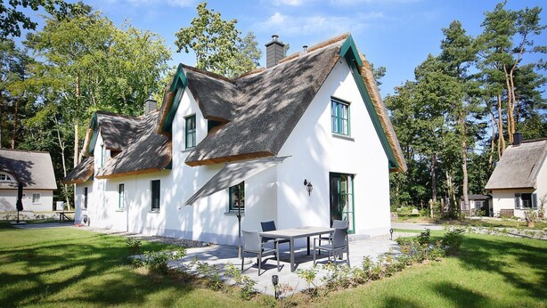 Ein traditionelles weißes Haus mit einem Reetdach, einer kleinen Terrasse mit Tisch und Stühlen sowie einem gepflegten Garten.