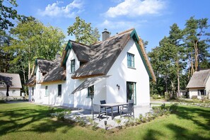 A traditional white house with a thatched roof, a small patio with a table and chairs, and a well-maintained garden.