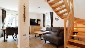 Ein modernes Wohnzimmer mit Holztreppe, einem Flachbildfernseher, einer Couch und einem Essbereich mit Stühlen.